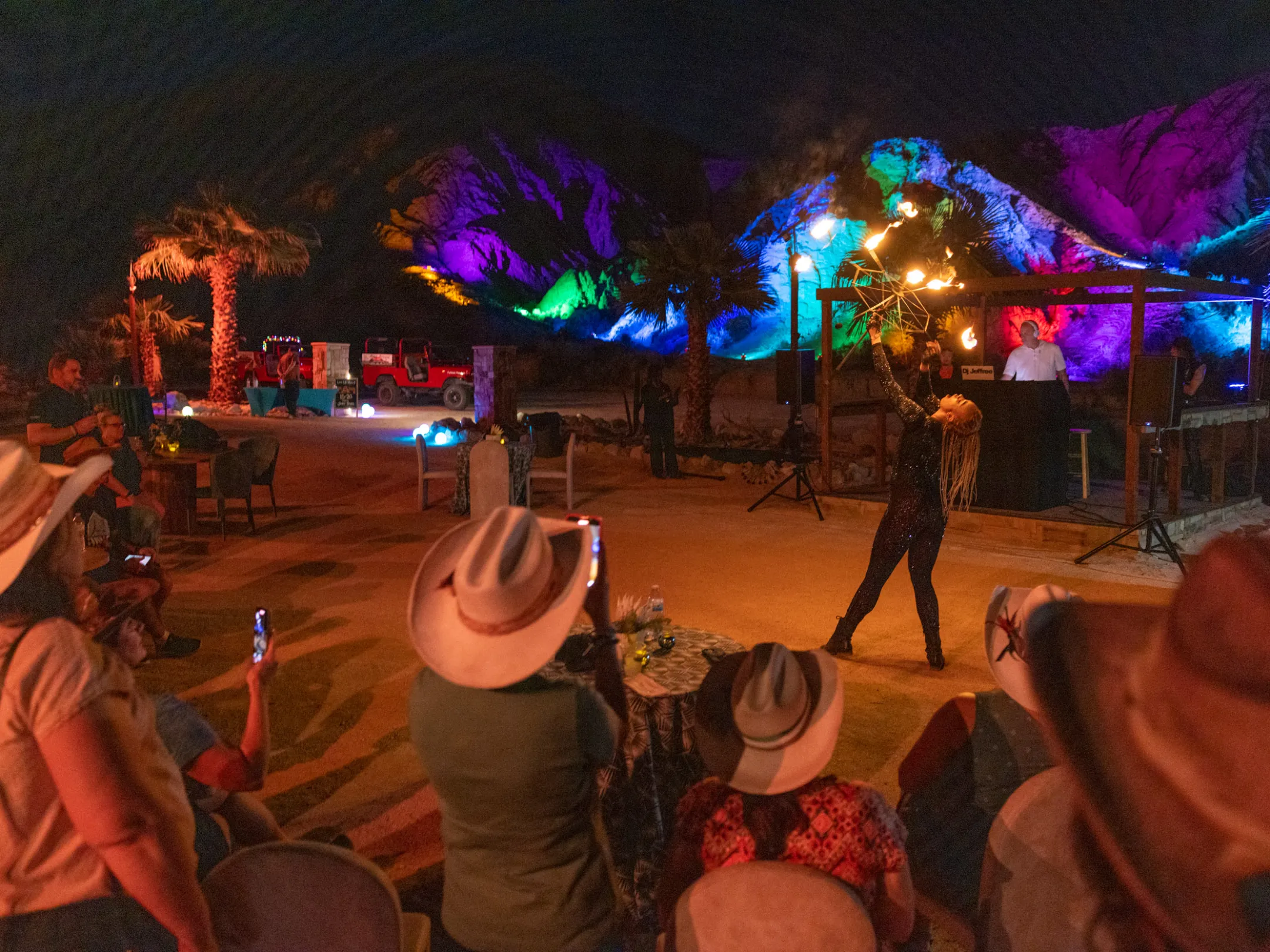 Performer twirling fire in front of audience with illuminated hills in background.