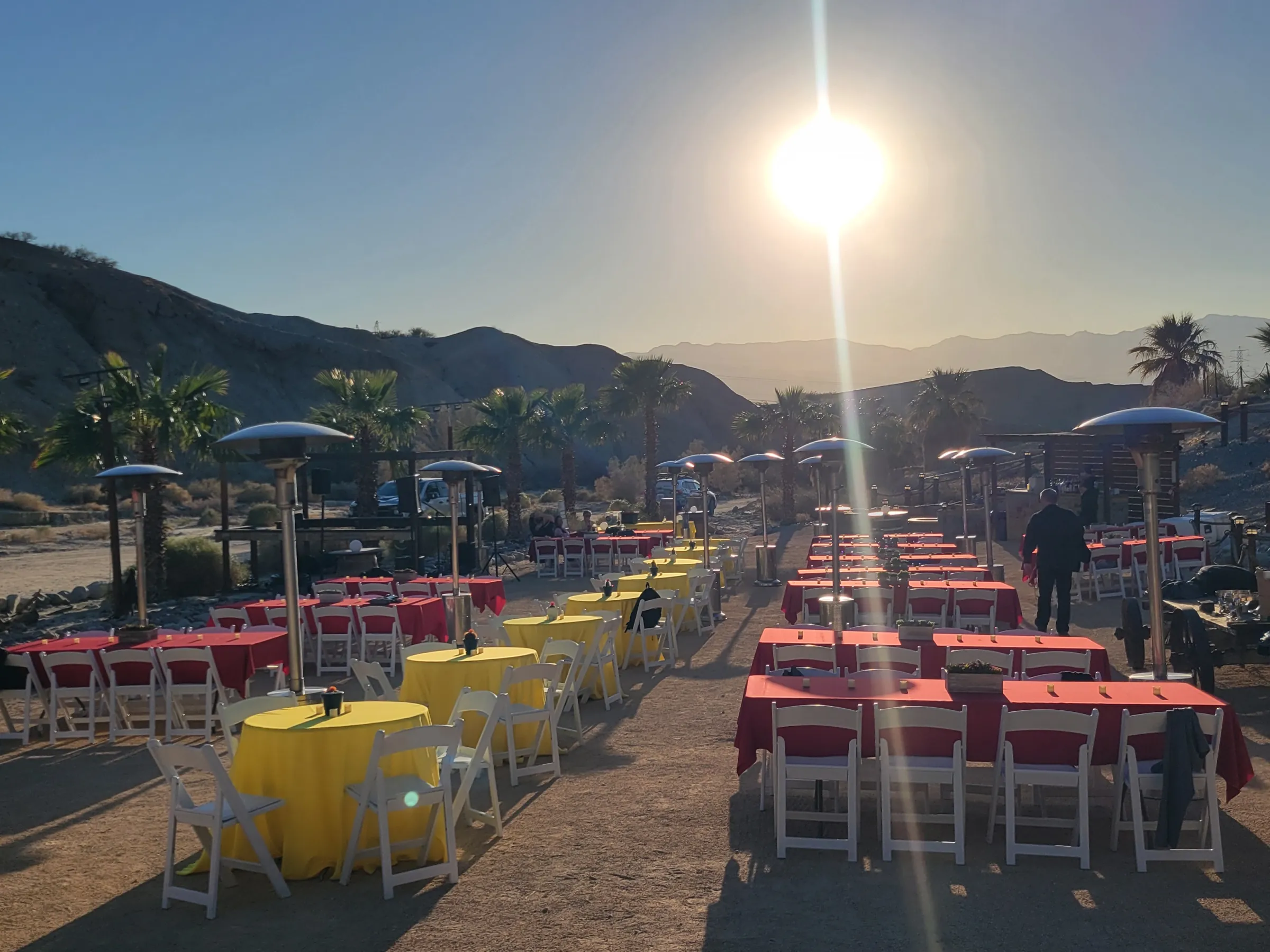 Outdoor event setup with tables, chairs, and heaters at sunset, surrounded by desert scenery.