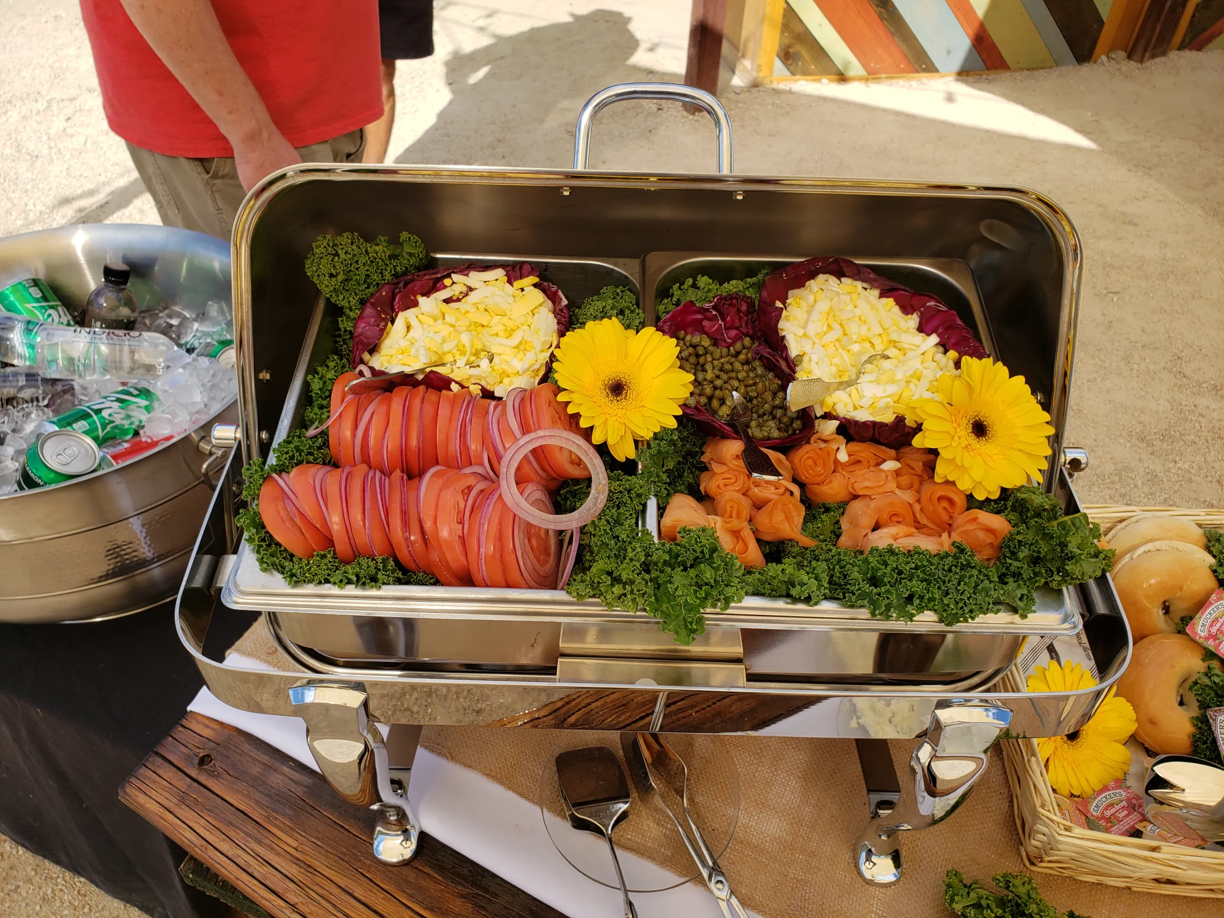Buffet tray with sliced tomatoes, smoked salmon, eggs, capers, and yellow flowers.