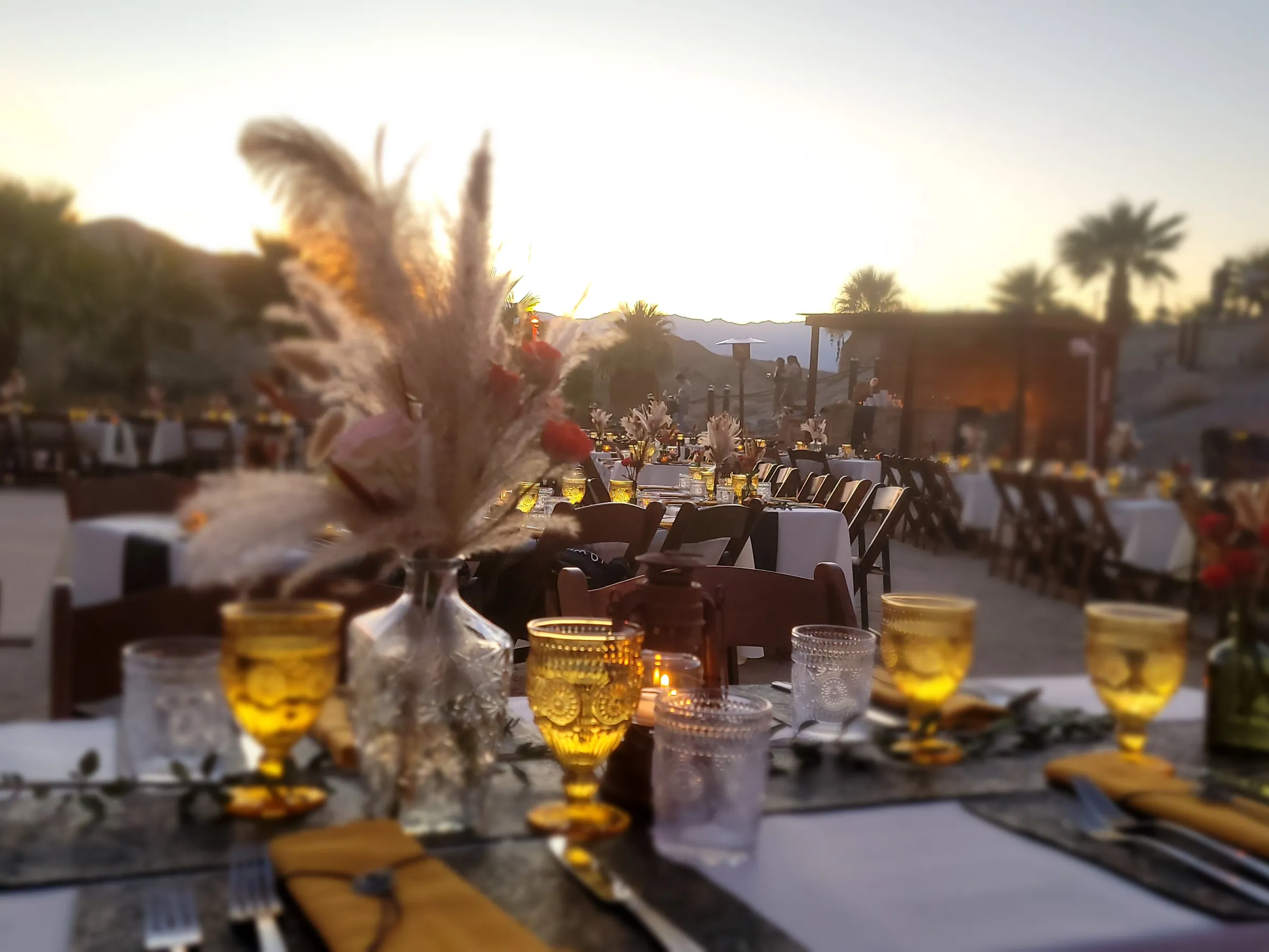 Outdoor event setup with decorated tables and chairs under a sunset sky.