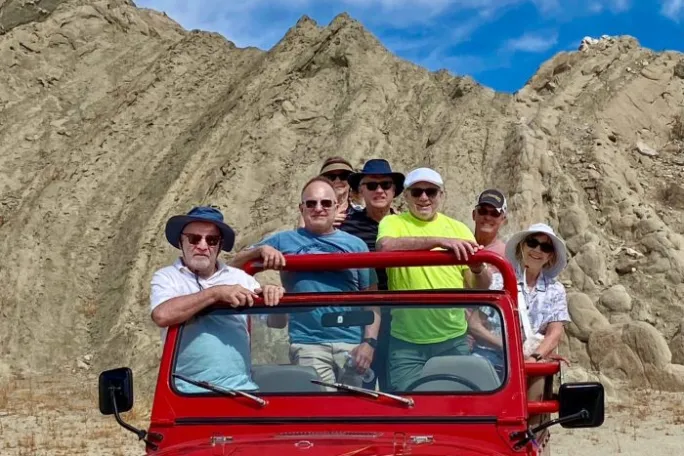 Group of people in and by a red jeep with rocky hills in the background.