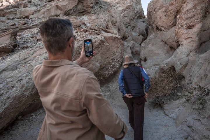 Man photographing woman hiking in rocky canyon.