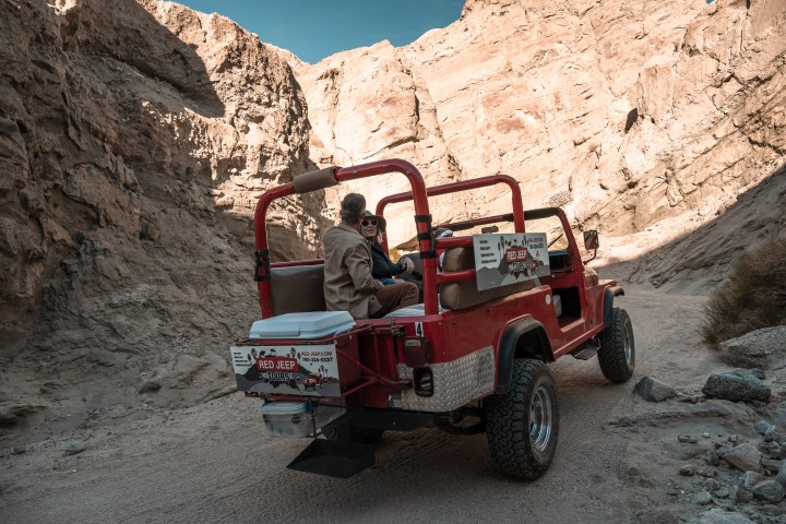 Man driving red open-top jeep in a rocky canyon.