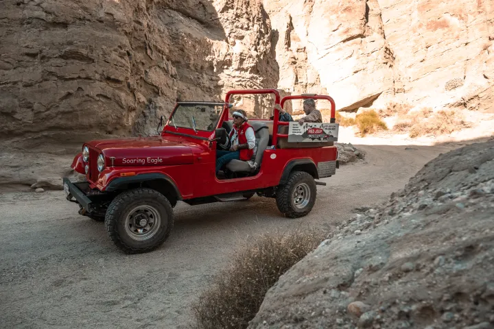 Red open-top jeep with two passengers driving through a rocky canyon.