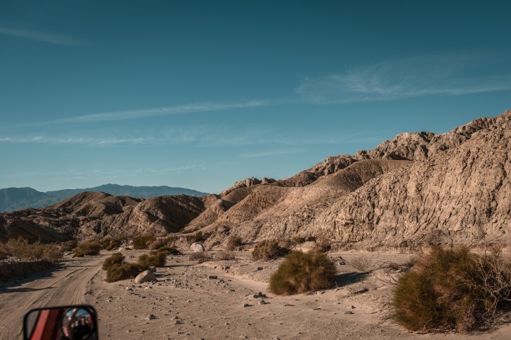 Desert landscape with dirt road and rocky hills under a clear blue sky.