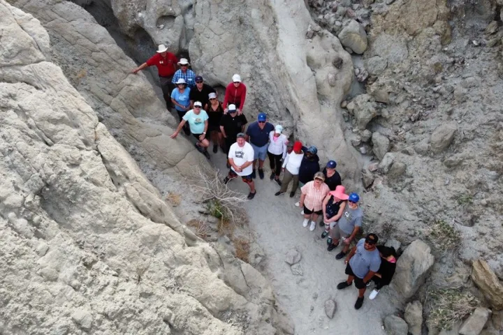 Group of people standing in a narrow rocky canyon, viewed from above.