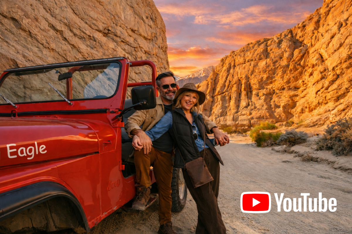 Couple smiling by a red Jeep in a desert canyon with sunset.